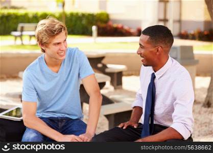 Teacher Sitting Talking To Male High School Student Outside