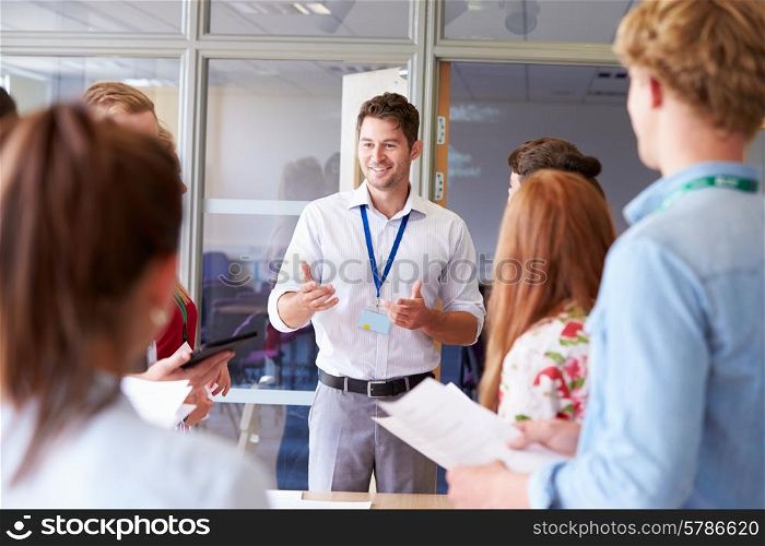Teacher With College Students Standing By Desks In Classroom