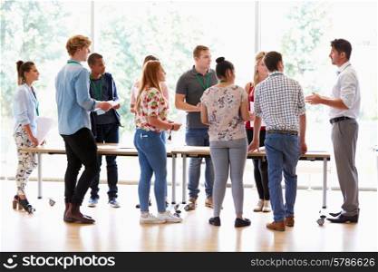 Teacher With College Students Standing By Desks In Classroom