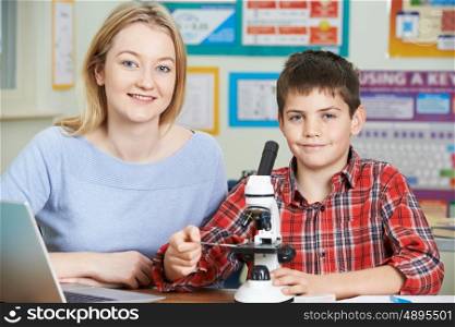 Teacher With Male Student Using Microscope In Science Class