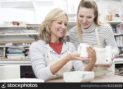 Teacher With Mature Woman Making Mug In Pottery Class