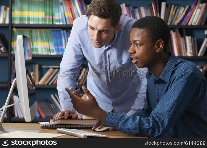 Teacher Working With Male Teenage Pupil At Computer