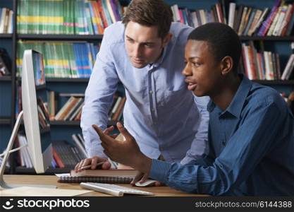 Teacher Working With Male Teenage Pupil At Computer
