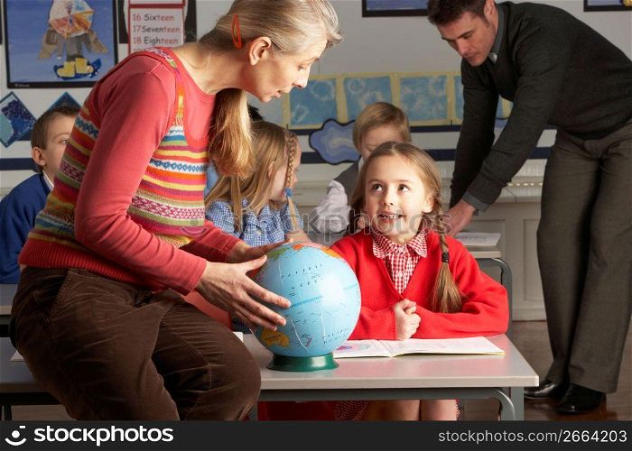 Teachers Giving Geography Lesson To Primary School Children In Classroom