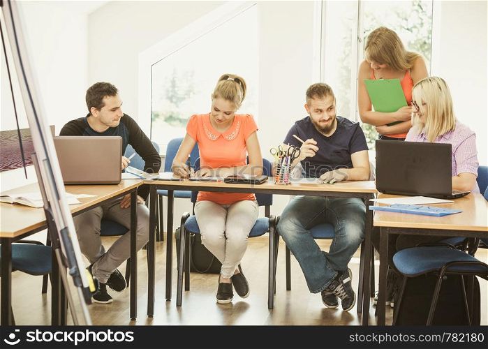 Teaching Concept. Female young teacher or tutor with adult students in classroom with papers, laptop computer. Studies course. Students and teacher tutor in classroom
