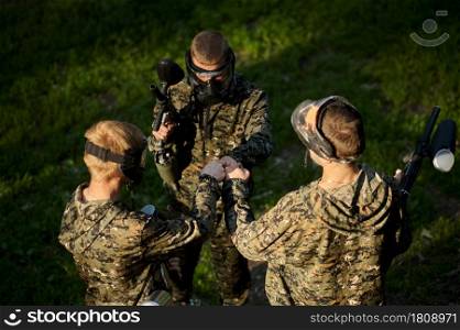 Team in camouflages and masks playing paintball, battle on playground in the forest. Extreme sport with pneumatic weapon and paint bullets or markers, military game outdoors, combat tactics. Team playing paintball, battle in the forest