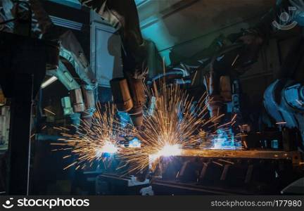 Team industrial robots are welding metal part in factory