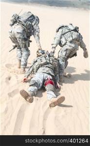 Team of airborne infantry paratroopers saving life of injured brother in arms dragging carrying him on desert sand. No man left behind. United states paratrooper airborne