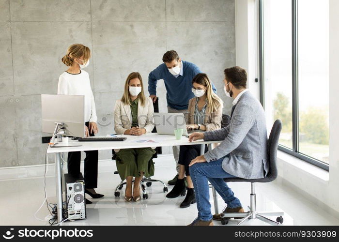 Team of business people working on project with facial masks as a virus protection in the office