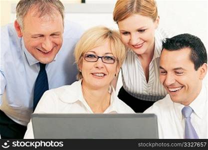 Team of four business people working in front a computer looking at the screen, seeing something good obviously