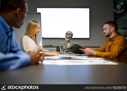 Team of managers and skeleton, conference in IT office, joke. Professional teamwork and planning, group brainstorming and corporate work, meeting of colleagues. Team of managers and skeleton in IT office, joke