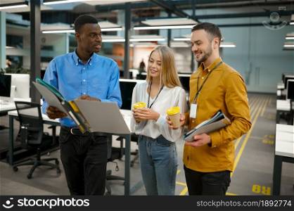 Team of managers with coffee talks in IT office. Professional teamwork and planning, group brainstorming and corporate work, modern company interior on background. Team of managers with coffee talks in IT office