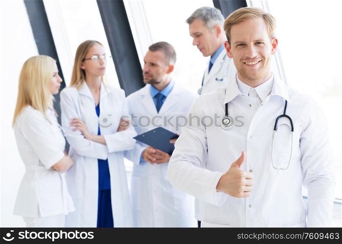 Team of medical professionals, young doctor looking at camera, smiling, showing thumb up. Team of medical professionals