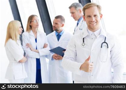 Team of medical professionals, young doctor looking at camera, smiling, showing thumb up. Team of medical professionals
