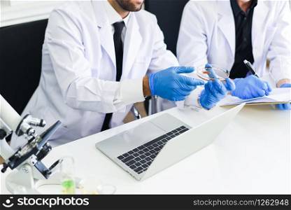 Team of scientist research are working in laboratory / Male doctor researcher are doing investigations with microscope and laptop in lab biochemistry genetics forensics blood test results concept