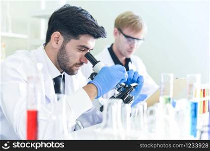 Team of scientist research working together conduct experiments and looks on microscope in modern laboratory / Scientists in lab biochemistry genetics forensics microbiology and test tube -