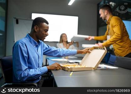 Team of workers eats pizza, business lunch in IT office. Professional teamwork and planning, group brainstorming and corporate work, modern company interior on background. Workers eats pizza, business lunch in IT office