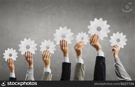 Teamwork and collaboration concept. Group of business people with raised hands holding cogwheels