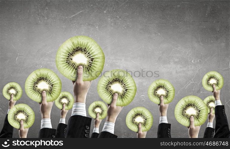 Teamwork and creativity concept. Group of business people holding kiwi slice in raised hands