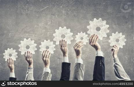 Teamwork concept. Group of business people with raised hands holding cogwheels
