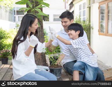 Teamwork of caucasian father, asian mother and young son leaning to plant tree in pot at front yard at home, happy young family have leisure time in weekend.