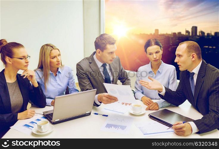 teamwork, technology and people concept - smiling business team with laptop computers, documents and coffee having discussion in office over city background. business team with laptop having discussion