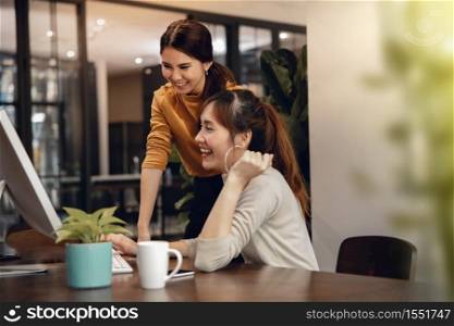 Teamwork, Working Together. Smiling Two Business Woman Workigng on Computer in Modern Office. Eyes focus on the screen