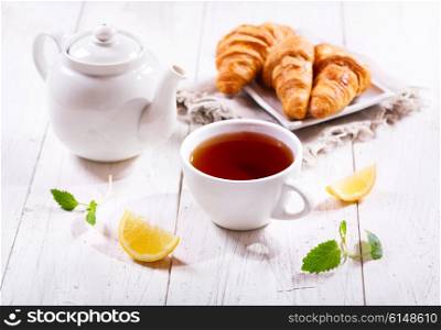 Teapot and cup of tea with mint and lemon on wooden table