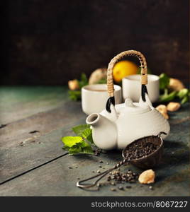 Teapot and cups of tea with mint and lemon on wooden table