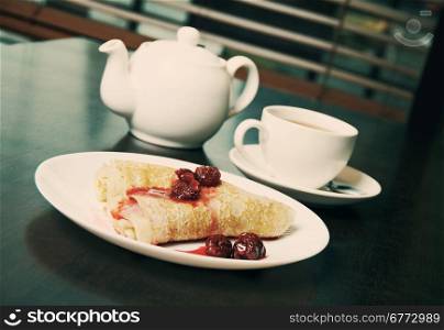 teapot, cup of tea and pancakes on plate with sweet cherry confiture