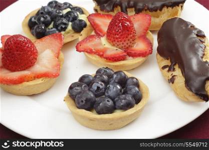 Teatime treats of homemade tarts filled with confectioner&rsquo;s custard and topped with fresh strawberries or blueberries, and chocolate eclairs.