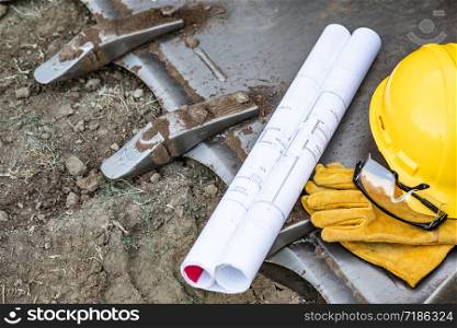 Technical Blueprints, Hardhat, Gloves and Protective Glasses Resting on Bulldozer Bucket Abstract