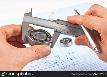 Technical drawing and callipers with bearing in hand on graph paper