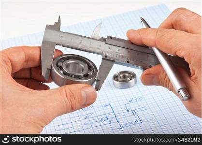 Technical drawing and callipers with bearing in hand on graph paper