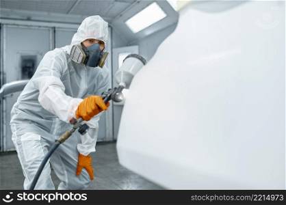 Technician hand in safety clothing spraying paint and varnish on car body part. Technician in safety clothing spraying car paint
