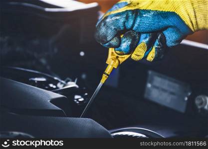 Technician hand pulling oil dipstick for checking lubricating oil level of the car engine