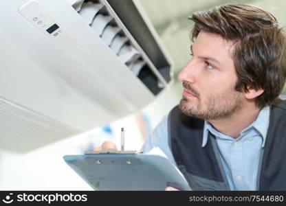 technician holding clipboard and inspecting air conditioning unit