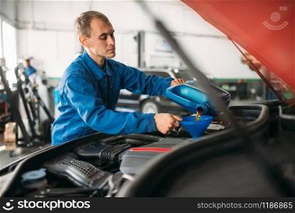 Technician pours new oil into the car engine. Vehicle engine maintenance, auto-service. Technician pours new oil into the car engine