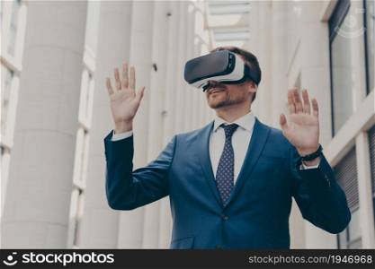 Technologies of future for your business. Europian businessman using VR headset for virtual reality game or work, wears 3d goggles and gesturing while working in augmented reality outdoors. Businessman using VR headset for virtual reality game for work, standing outdoors
