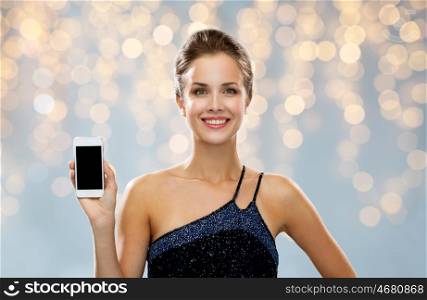technology, advertisement, holidays and people concept - smiling woman in evening dress with blank smartphone screen over black background