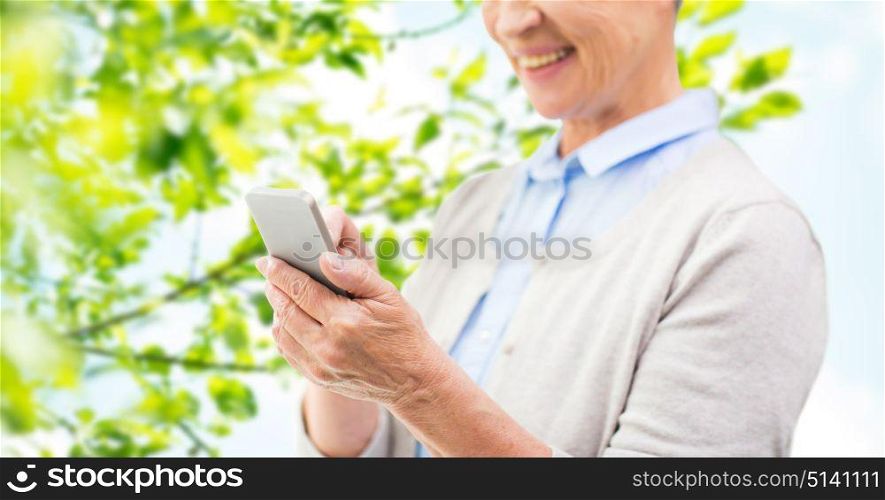 technology, age and people concept - close up of happy senior woman with smartphone texting message over green natural background. close up of senior woman with smartphone texting