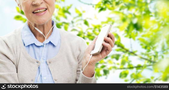 technology, age and people concept - close up of happy senior woman with smartphone and earphones listening to music over green natural background. happy senior woman with smartphone and earphones