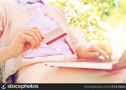 technology, age and people concept - close up of senior woman with laptop compute and credit or bank card over green natural background. senior woman with laptop and credit card