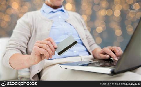 technology, age and people concept - close up of senior woman with laptop compute and credit or bank card shopping online over holidays lights background. senior woman with laptop and credit card