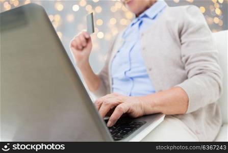 technology, age and people concept - close up of senior woman with laptop compute and credit or bank card shopping online over holidays lights background. senior woman with laptop and credit card