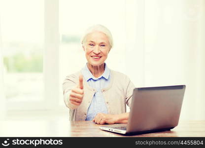 technology, age and people concept - happy senior woman with laptop computer at home showing thumbs up gesture