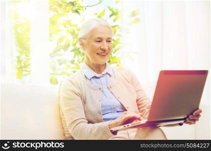 technology, age and people concept - happy senior woman with laptop computer at home over window with green natural background. happy senior woman with laptop at home. happy senior woman with laptop at home