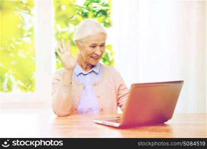 technology, age and people concept - happy senior woman with laptop computer having video chat at home and waving hand over window with green natural background. senior woman with laptop having video chat at home. senior woman with laptop having video chat at home