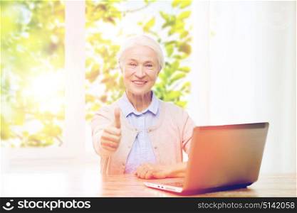 technology, age and people concept - happy senior woman with laptop computer at home showing thumbs up gesture over green natural background. happy senior woman with laptop showing thumbs up