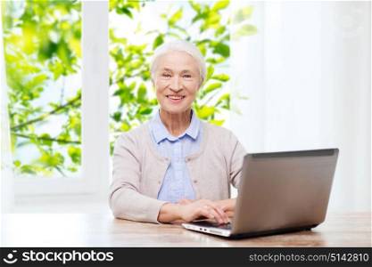 technology, age and people concept - happy senior woman with laptop computer at home over window and green natural background. happy senior woman with laptop at home